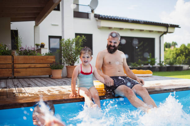 istock Father with three daughters outdoors in the backyard, sitting by swimming pool. 1337578704