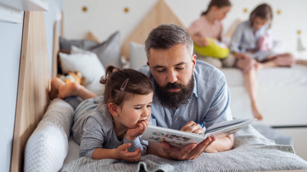 istock Father with three daughters indoors at home, reading a book. 1337578783
