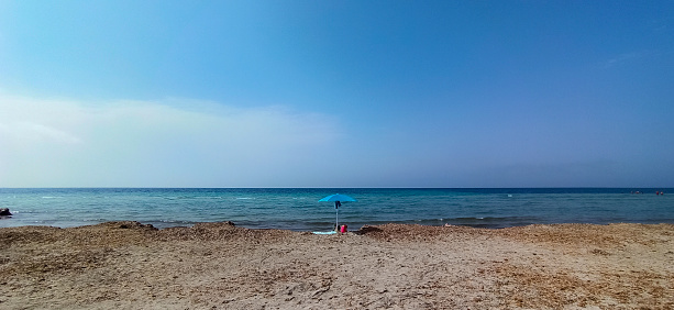 lonely umbrella on empty beach with blue sea. Capo feto, Sicily. Italy