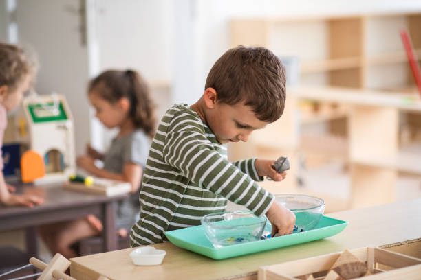 Small nursery school boy playing indoors in classroom, montessori learning. Small concentrated nursery school boy playing indoors in classroom, montessori learning. montessori stock pictures, royalty-free photos & images