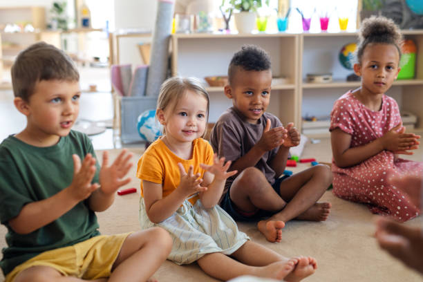Group of small nursery school children sitting on floor indoors in classroom, clapping. A group of small nursery school children sitting on floor indoors in classroom, clapping. child care stock pictures, royalty-free photos & images