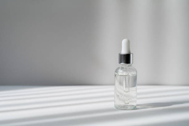 istock Serum in transparent bottle with white and silver cap on the grey background in with light and shadow stripes. Essence in glass dropper bottle. Skin care cosmetic product for branding. Copy space 1337580275