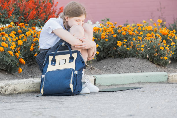 Sad desperate young girl suffering from bulling and harassment felling lonely, unhappy desperate and hopeless sitting outdoors. School isolation, abuse and bullying concept stock photo