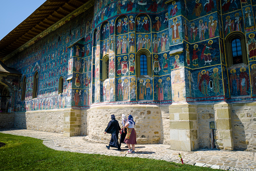 Moldovita, Romania - 5 August, 2021: Color image depicting people outside the ancient architecture and murals of Moldovita monastery in the north of Romania.