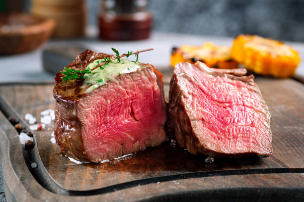 ein großes gegrilltes filet mignon steak mit butter und thymian wird gehackt auf einem holzbrett serviert. ein gericht aus gebratenem fleisch in nahaufnahme - steak stock-fotos und bilder