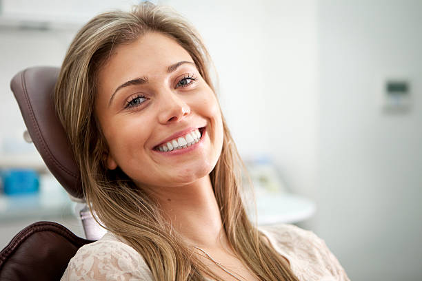 Bright smile from the Dentist's Chair A bright toothy smile and eye contact from a pretty young woman proud to show off her perfect teeth while sitting in a dentist's chair. dentists chair stock pictures, royalty-free photos & images