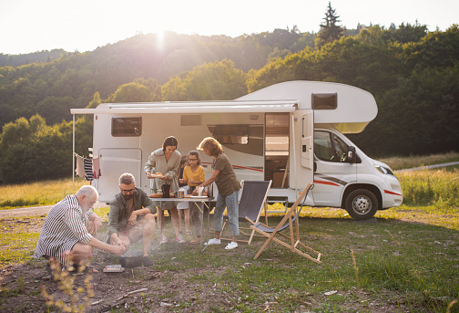 Familia de varias generaciones sentada y comiendo al aire libre en coche, viaje de vacaciones en caravana. photo