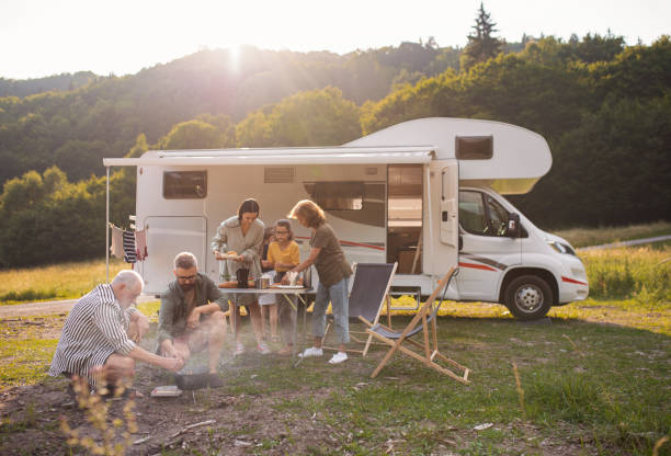 multi-generation family sitting and eating outdoors by car, caravan holiday trip. - acampando imagens e fotografias de stock