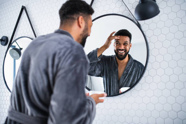 istock Young man applying cream on face indoors at home, morning or evening routine concept. 1337586501