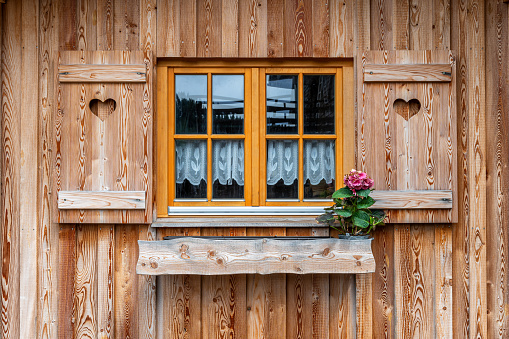 Close-up of the façade of an old house with weathered windows and flowering potted plants, Aosta, Italy