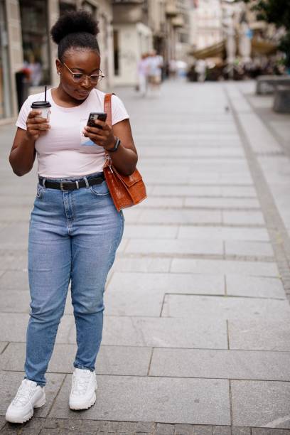 istock Young woman using smart phone while drinking coffee to go on a city street 1337588971