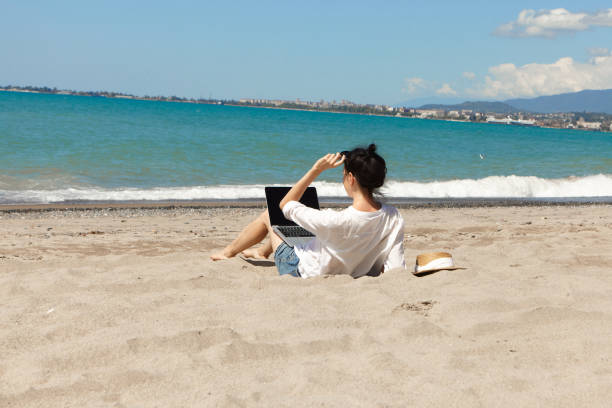istock Young woman using laptop computer on a beach. Vacation lifestyle communication. Freelance work concept 1337591755