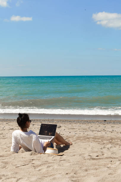 istock Young woman using laptop computer on a beach. Vacation lifestyle communication. Freelance work concept 1337594134