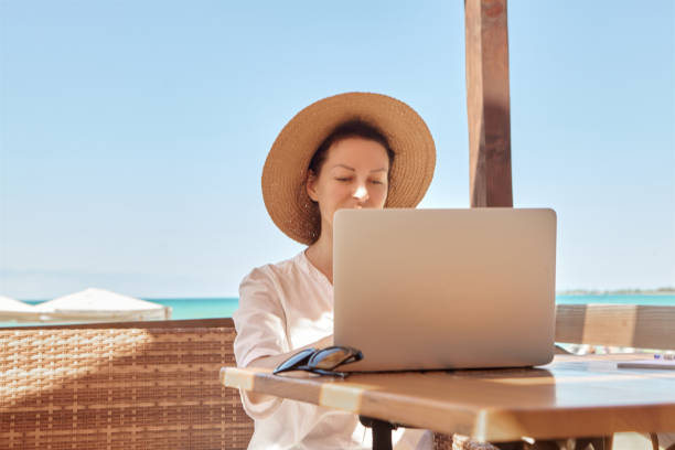 istock Young woman using laptop computer on a beach. Freelance work concept.Pretty young woman using laptop in cafe on tropical beach in outdoor cafe terrace with sea view. Work and travel 1337594157