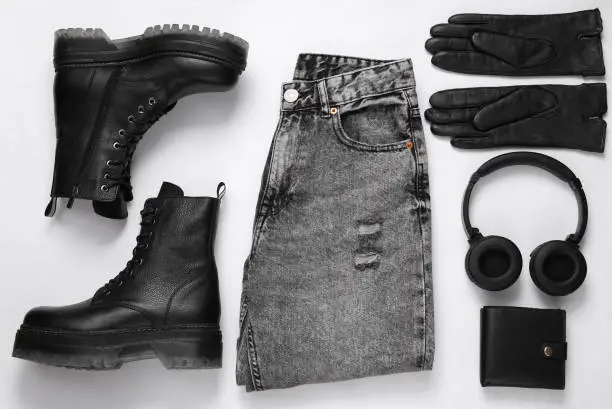 Photo of Women's clothing and accessories. Jeans and leather black boots, gloves, purse, headphones on a white background. Top view