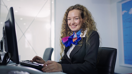 Smiling friendly female staff at check in counter using keyboard and computer looking at camera.