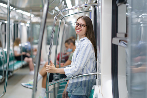 Cheerful young girl inside metro carriage student return home after successful exam in university. Smiling female lean at door in underground happy to travel subway after lockdown without restrictions