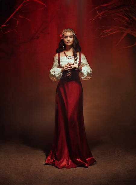 Young beautiful gypsy woman stands in a dark room. Long black flowing hair, rose hairpin. Red ethnic vintage dress, fortune teller costume. Gold jewelry. Mystical fantasy girl, pagan witch. Art photo Young beautiful gypsy woman stands in a dark room. Long black flowing hair, rose hairpin. Red ethnic vintage dress, fortune teller costume. Gold jewelry. Mystical fantasy girl, pagan witch. Art photo. fortune teller photos stock pictures, royalty-free photos & images
