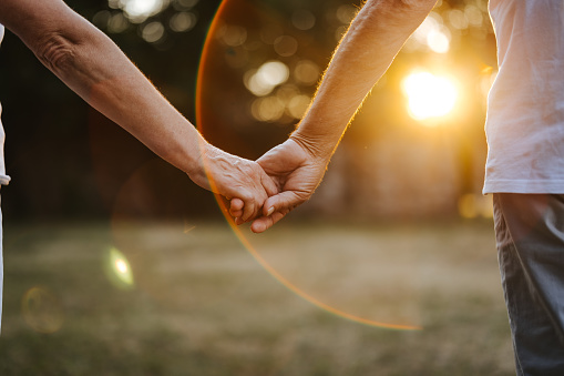 Close-up shot of senior couple holding hands in nature at sunset