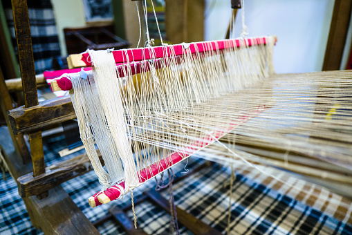 Close up of the cotton yarn which is being woven by a loom.