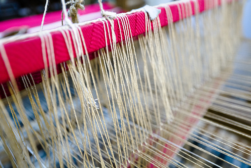 Close up of the cotton yarn which is being woven by a loom.