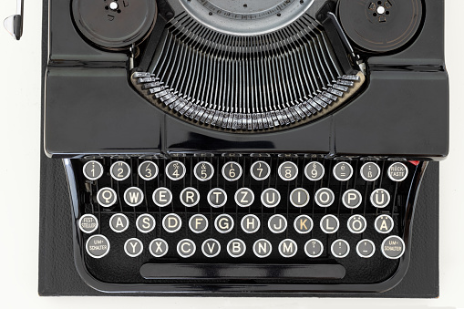 Close up of 1940's manual typewriter from several different angles.  Typewriter sitting on a brown desk with light coming in through shutters.  Brown typewriter body with green keys.