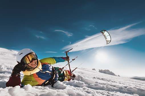 Adult kite surfer lies on the snow with kite in hand and smile. Snowkiting concept with ski or snowboard