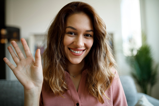 Young smiling woman waving with hand on video call at home office