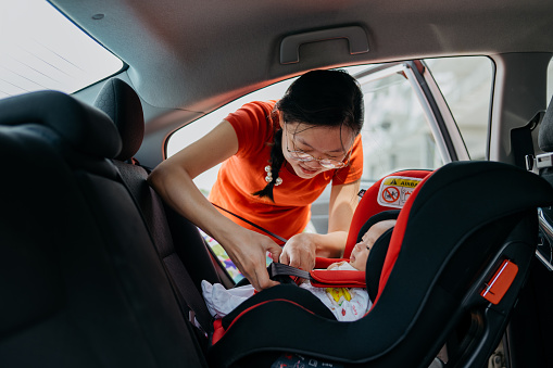 Image of an Asian Chinese woman fastening seat belt for her baby boy on car safety seat before driving