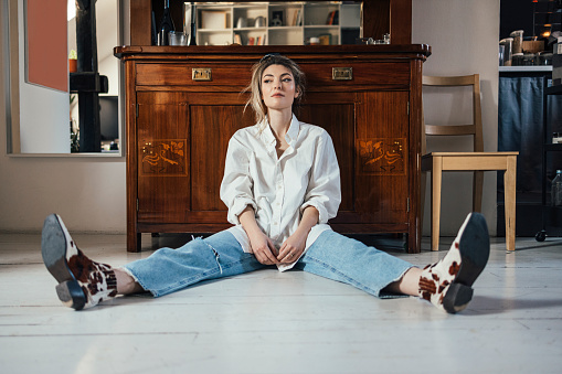 Serious female sitting on white wooden floor and looking away