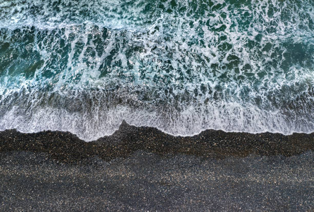 istock Stormy waves with white sea foam breaking on dark sandy beach, view from directly above 1337645625