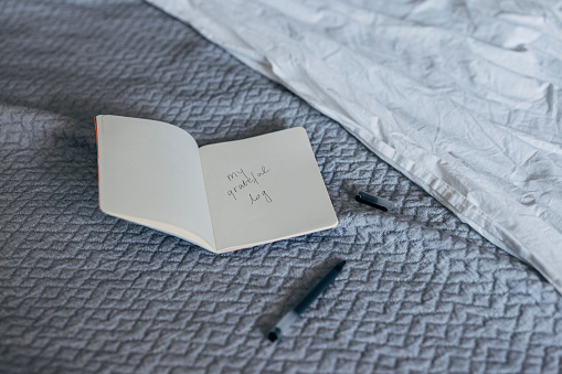 Notebook and black pen on a bed with gray blanket in a hotel room