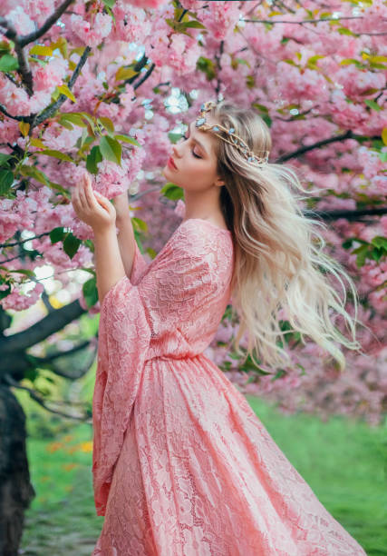 fantasia mulher feliz princesa caminha na primavera florescendo jardim abraça-se por ombros. flores rosas sakura tree natureza verão. longo vestido de renda mangas largas voa em movimento do vento. rainha loira. - wind textile women retro revival - fotografias e filmes do acervo