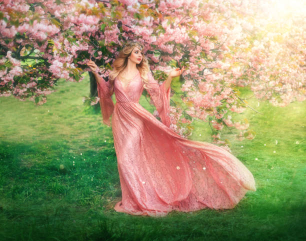 Fantasy happy girl elf princess walks in spring blooming garden. Pink flowers sakura tree green grass summer nature. long lace dress wide sleeves flies in wind motion. Blonde woman queen. vintage gown fantasía feliz niña elfa princesa camina en el jardín floreciente de primavera. flores rosas sakura árbol hierba verde verano naturaleza. vestido largo de encaje mangas anchas vuela en movimiento de viento. mujer rubia reina. vestido vintage
