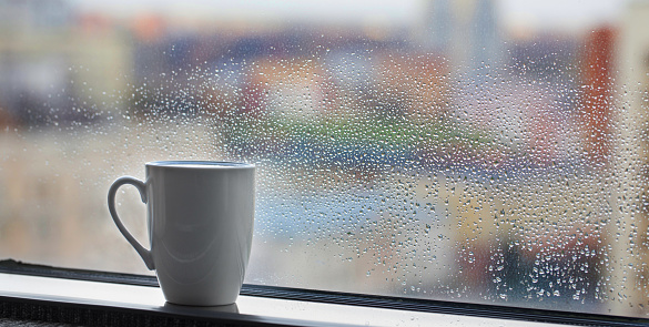 cup of coffee on windowsill with raindrops on glass