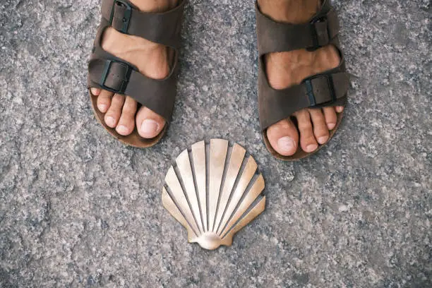 the legs of a pilgrim on sandals and the shell signal in an ancient city of Spain