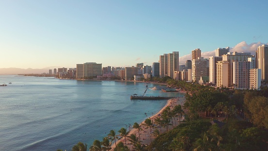 Panning aerial drone slowly flying over a colorful Honolulu Skyline while Sunset in Oahu, Hawaii with Waikiki Beach Shooting from a bird's eye view. Magnificent mountains of Hawaiian island of Oahu