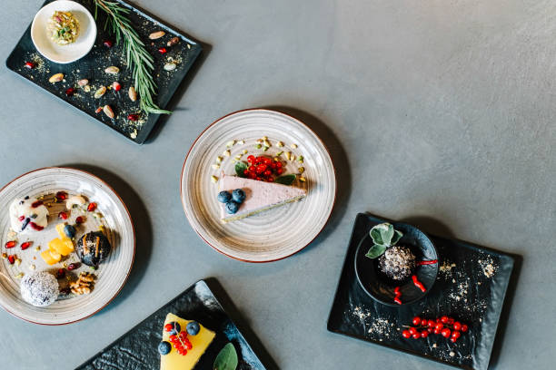 Directly above photo of sugar free desserts with fruits and nuts: few healthy energy balls and fruit cakes served on black plates in a restaurant table with copy space, raw food and healthy eating concept.