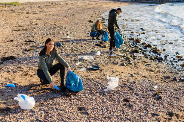 istock Dedicated woman in a team picking up plastic garbage in bag at beach 1337667683
