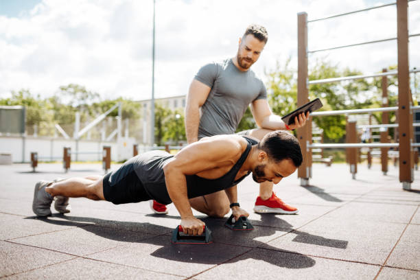 Fitness instructor with athlete on outdoor strength training doing push ups Fitness instructor with client on training outdoors fitness trainer stock pictures, royalty-free photos & images