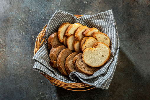 Slices of white bread with whole grain bread in a small wicker basket on colored background.