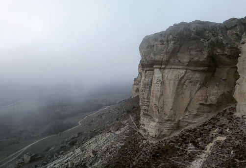 Steep cliffs with a misty gloomy sky. A thick, eerie fog hangs over the mountain and the valley.
