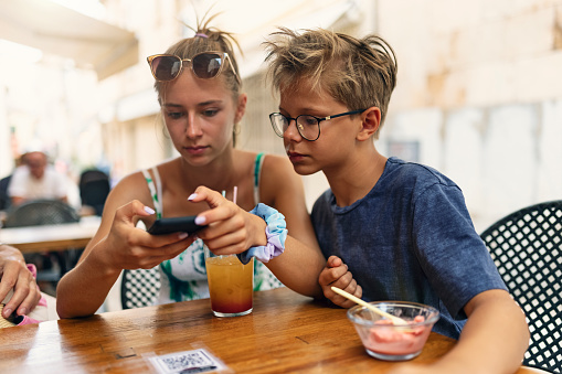 Brother and sister checking mobile menu at sidewalk café in Alcudia, Majorca, Spain. Family has scanned the QR code on the table and they are reading the menu on the mobile phones.
Canon R5.