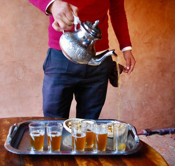 Man pouring Moroccan mint tea from a traditional metal teapot into glass cups