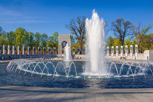 World War II Memorial in the Evening with Blue Sky and Clouds, Washington DC, USA. Green Trees, Water of the Fountain and Sightseeing Tourists are in the image. Canon EF 24-105mm/4L IS USM Lens.