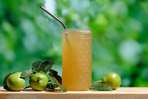 Pear juice on wooden table outdoors. Glass of juice and ripe pears fruits, green trees foliage on background. Healthy summer drinks concept.