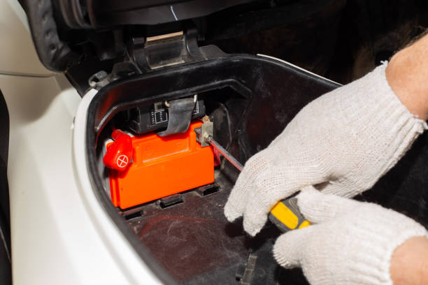istock A gloved auto mechanic with a screwdriver unscrews the motorcycle battery terminals for repair or replacement. Car service in a car service 1337703422