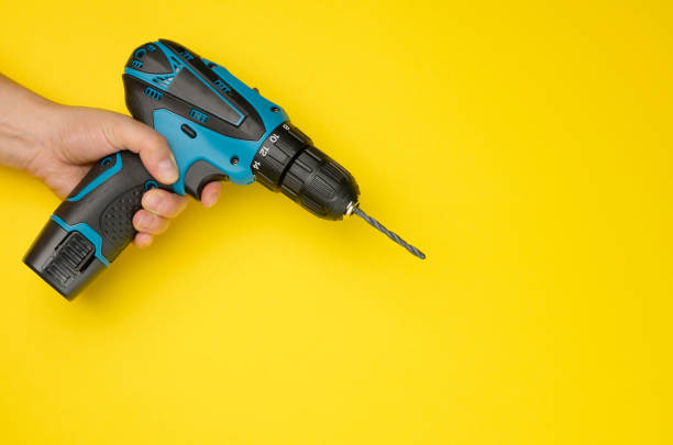 istock female hand holds a cordless drill on a yellow background. Tool for work 1337706089