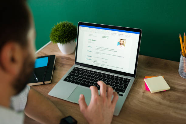 Young man updating his curriculum vitae Rear view of an adult man searching for a new job and working on writing his resume on the laptop good cv stock pictures, royalty-free photos & images