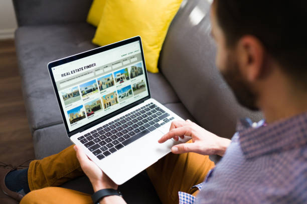 Man checking ads of houses for sale Rear view of a man looking for new houses on sale online. Young man using a real estate website on the laptop web page stock pictures, royalty-free photos & images